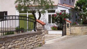 A stone wall with a metal gate, a white building with a tiled roof, and a tree with green foliage.