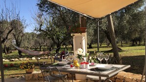 Un espace de restauration en plein air avec une table dressée pour deux personnes, entourée de chaises, d’un hamac et d’une lampe.
