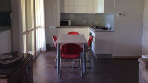 A modern kitchen with white cabinets, a microwave, and a gas stove. There is a dining table with red chairs and a window with curtains. - Sirmione Borgo Rosa, your holiday flat. Wifi. (Sirmione)