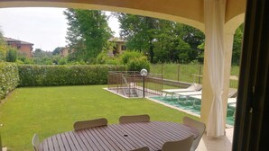A covered patio area with a round table and chairs, a swimming pool, and a view of the surrounding garden and buildings. - Sirmione Borgo Rosa, your holiday flat. Wifi. (Sirmione)