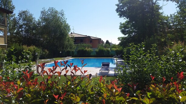 A swimming pool with lounge chairs, surrounded by greenery and a building in the background. - Sirmione Borgo Rosa, your holiday flat. Wifi. (Sirmione)