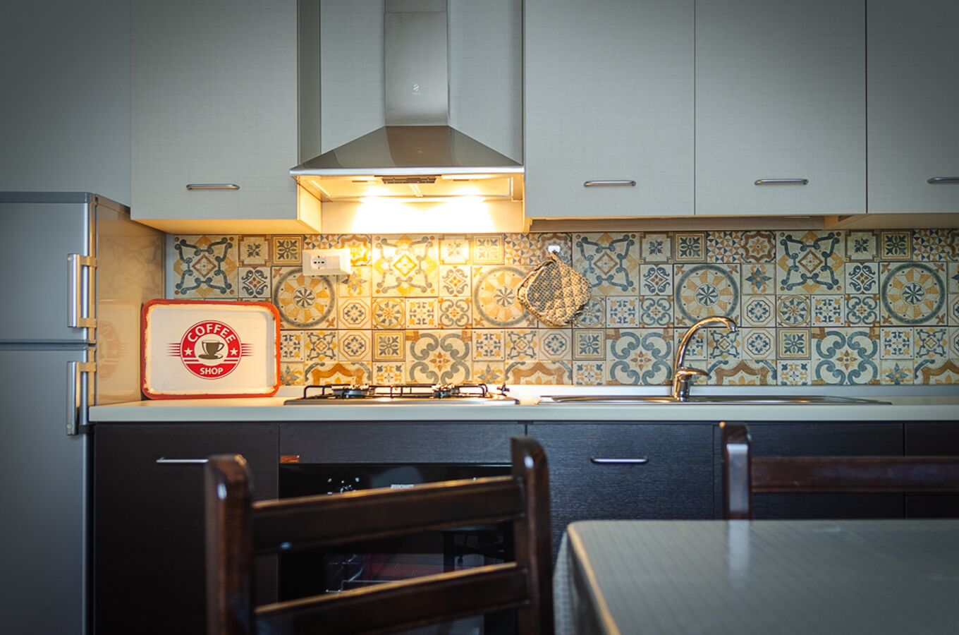 A kitchen with a tiled backsplash, a gas stove, and a coffee shop sign.