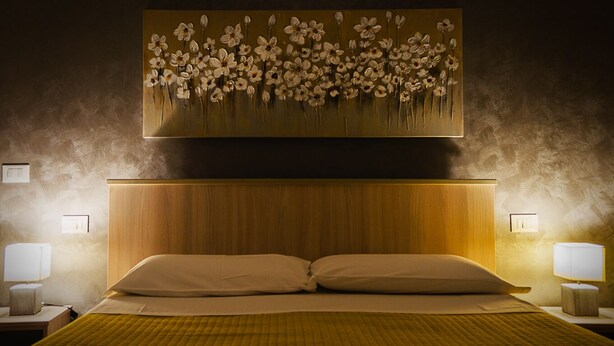 A hotel room with a large bed, two bedside lamps, and a wall-mounted painting of flowers. - Bice's House - Accommodation 3 (Cassibile)