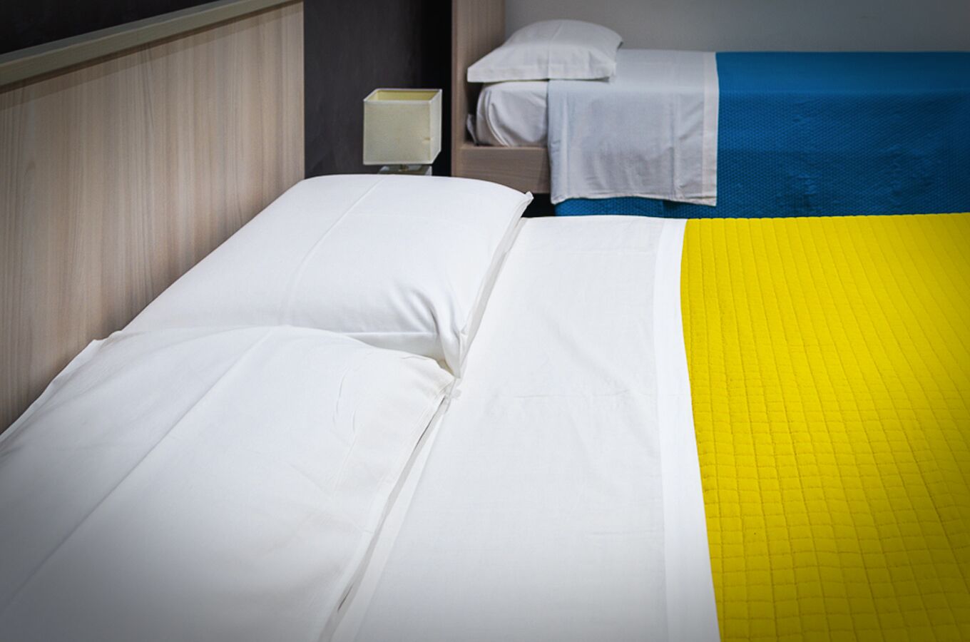 A hotel room with a bed, a nightstand, and a lamp.