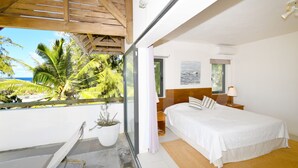 A bedroom with a bed, a nightstand, a window, and a view of palm trees. - Peters Beach House with pool, waterfront, Housekeeper who cooks your shopping (Poste Lafayette)