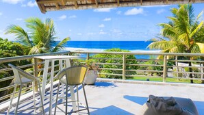 A balcony with chairs and a potted plant, overlooking a beach with palm trees and the ocean. - Peters Beach House with pool, waterfront, Housekeeper who cooks your shopping (Poste Lafayette)