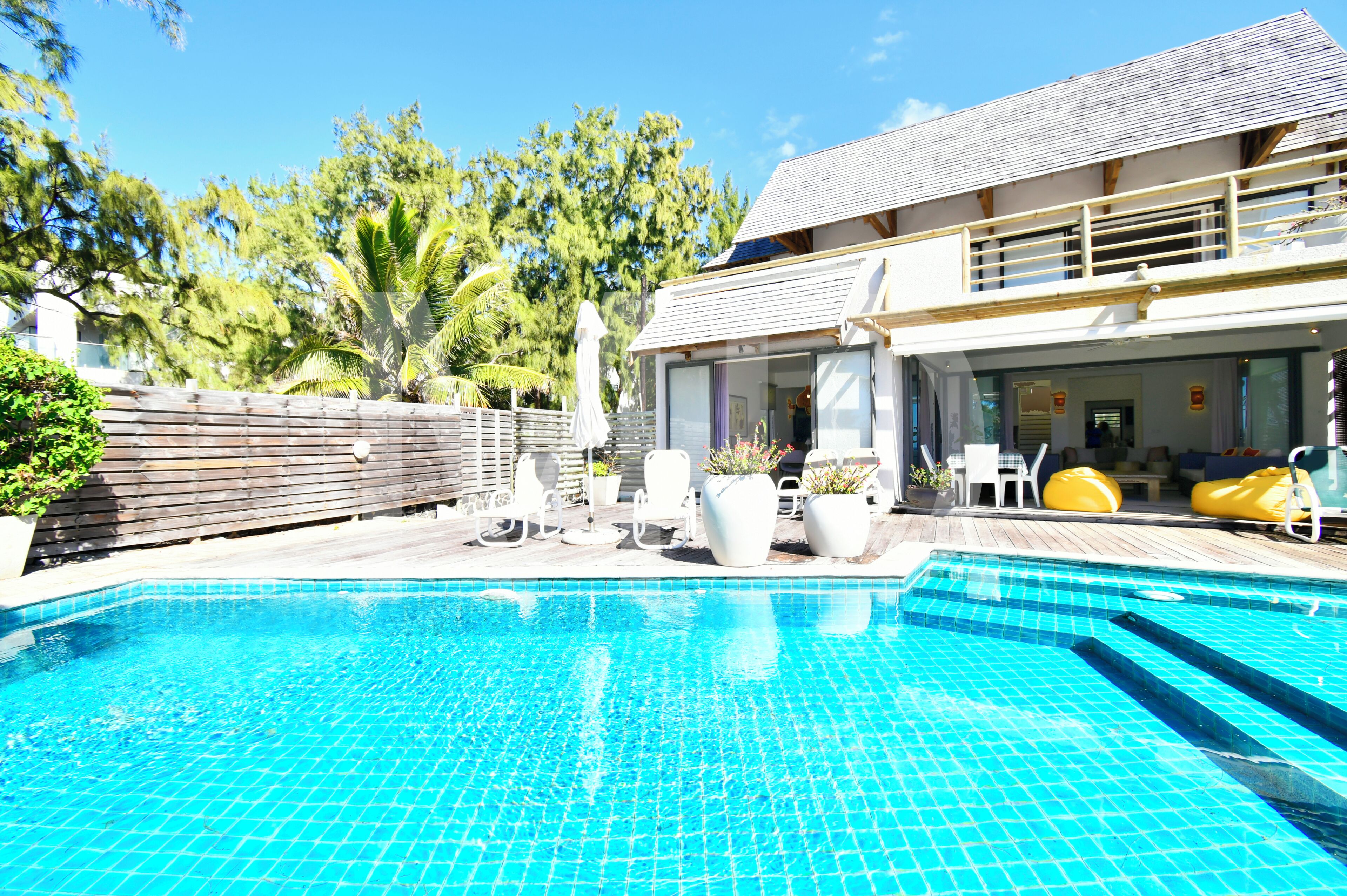 A swimming pool with tiled flooring, surrounded by outdoor seating and potted plants.