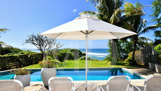 A poolside area with lounge chairs and a large umbrella, overlooking a clear blue ocean. - Peters Beach House with pool, waterfront, Housekeeper who cooks your shopping (Poste Lafayette)