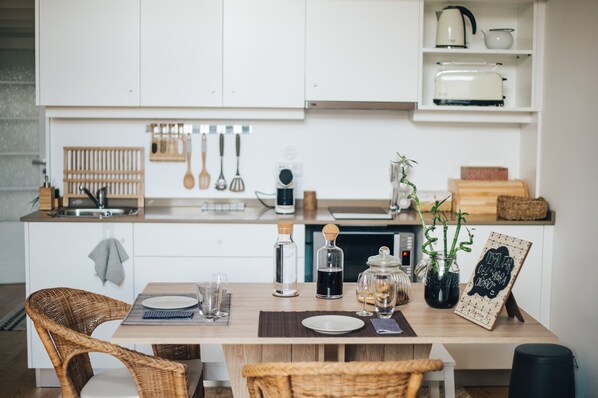 A modern kitchen with white cabinets, a wooden dining table, wicker chairs, and various kitchen utensils.
