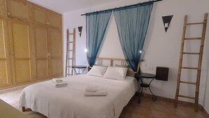 A bedroom with a bed, two nightstands, a wooden wardrobe, and a ladder.