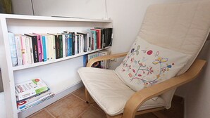 A room with a wooden chair with a floral cushion, a bookshelf filled with books, and a tiled floor.