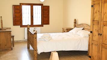 Een slaapkamer met een houten bed, nachtkastje, kledingkast en een raam met houten luiken.