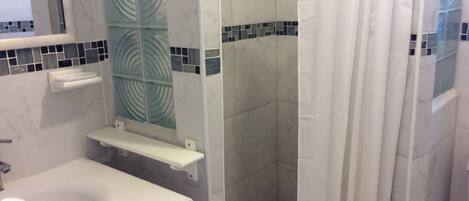 Un bagno con un lavandino bianco, uno specchio, una doccia con porta in vetro e un pavimento piastrellato.