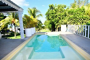 A swimming pool with a white fence and palm trees in the background.