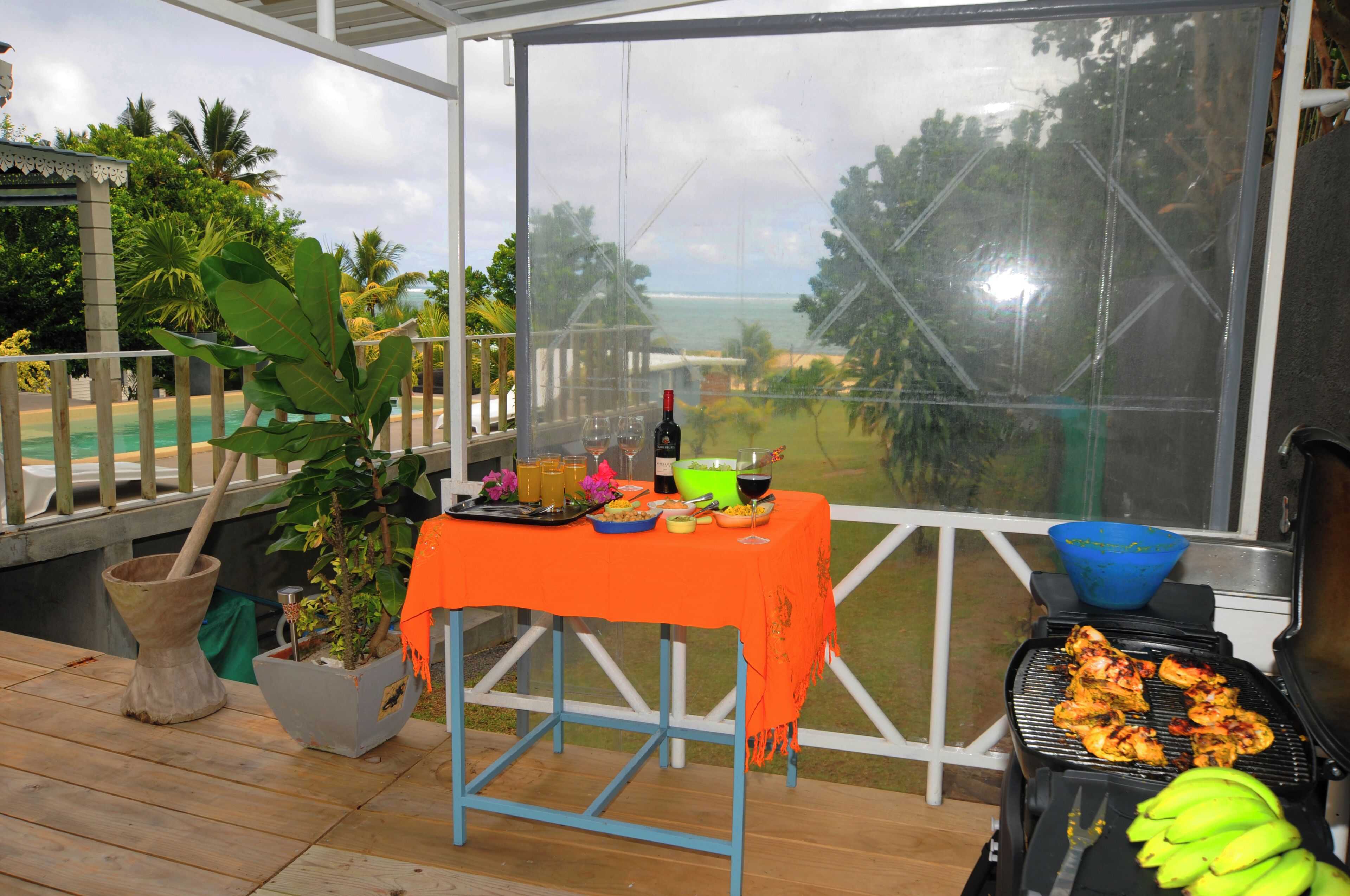 Un espace extérieur abrité, avec une table dressée pour un repas, un barbecue avec de la nourriture et une vue sur l’océan.