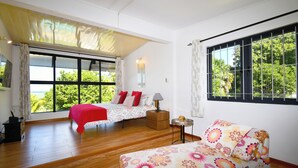 A bedroom with a bed, a sofa, a window with a view of greenery, a lamp, and a small table. - Riambel: Villa Antema, pool, right on the beach (Riambel)