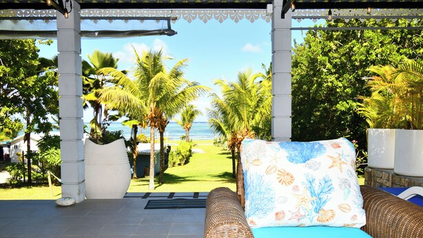 A covered outdoor seating area with a view of the ocean, a wicker sofa, and a decorative pillow. - Riambel: Villa Antema, pool, right on the beach (Riambel)