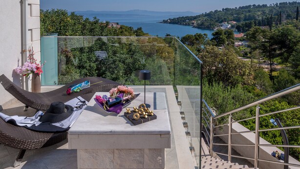 Un balcón con mobiliario de mimbre, una mesa con adornos y vistas a un lago y colinas.