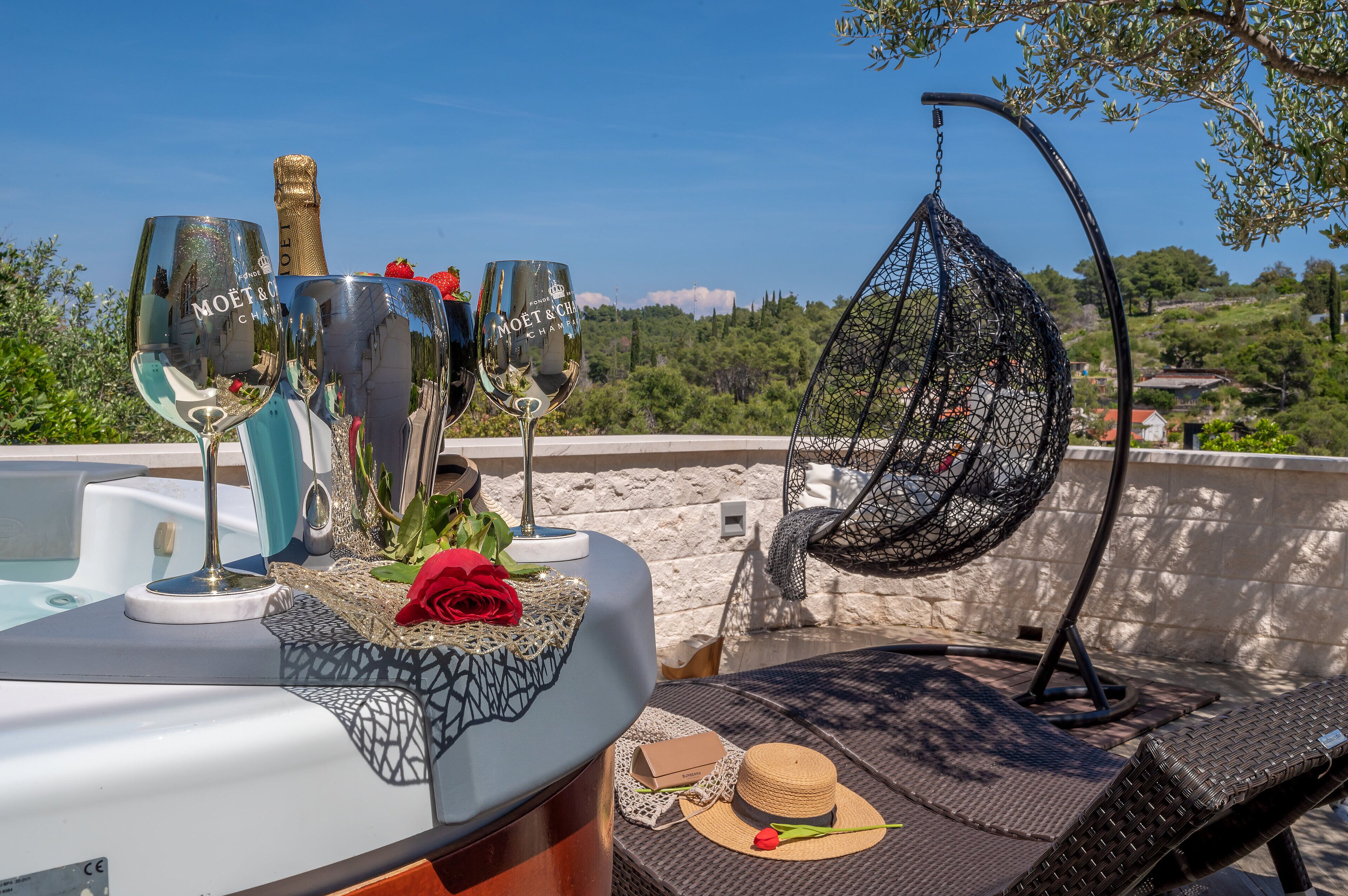 A terrace with a table set for two, featuring two champagne flutes, a bottle, and a decorative rose.