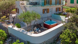 Una casa de dos plantas con piscina, muros de piedra y un balcón.