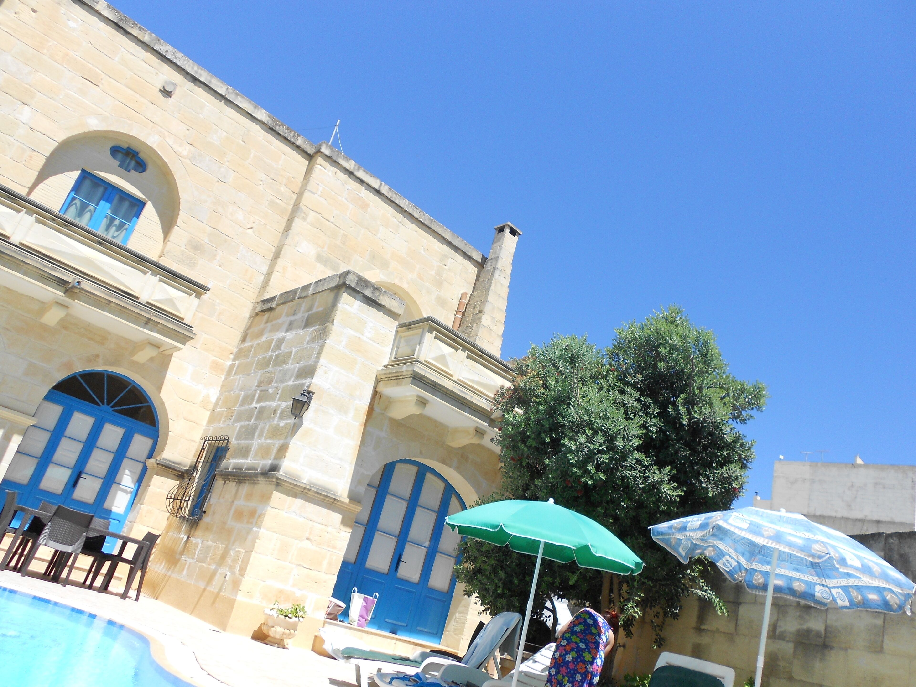 A stone building with blue doors and windows, a swimming pool, and outdoor seating.