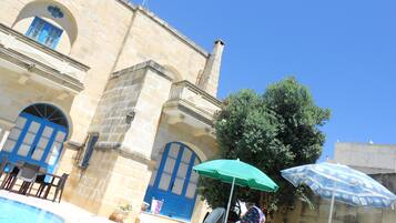 A stone building with blue doors and windows, a swimming pool, and outdoor seating.