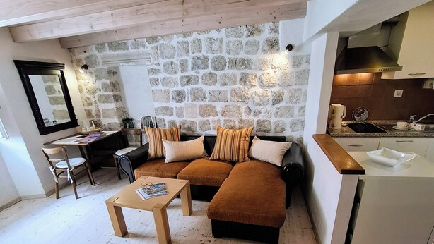 A modern living room with a stone wall, wooden flooring, and a kitchen area. - Ivo Apartment  in Dubrovnik Old Town (Dubrovnik)