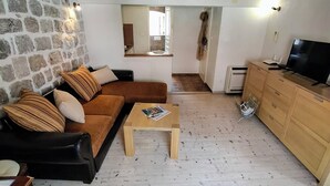 A living room with a stone wall, wooden beams, a brown sofa, a wooden coffee table, and a TV stand. - Ivo Apartment  in Dubrovnik Old Town (Dubrovnik)