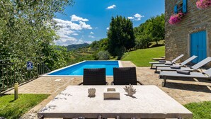 Un edificio de piedra con piscina, asientos al aire libre y vistas al campo.