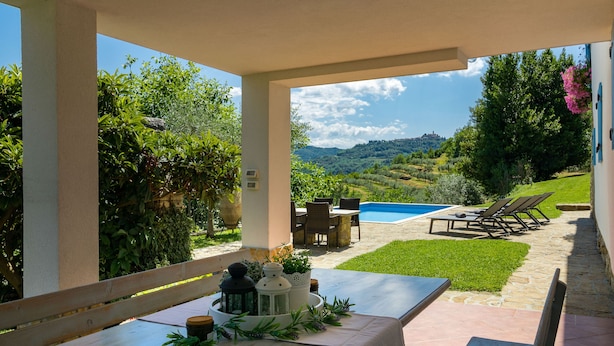 Un área de comedor al aire libre techada con piscina, sillas y vistas al campo.