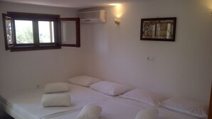 Un dormitorio con cama, almohadas, una ventana, aire acondicionado y una lámpara de pared.