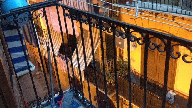 Un balcon avec une balustrade en métal, un pot bleu et un tissu rayé qui pend.