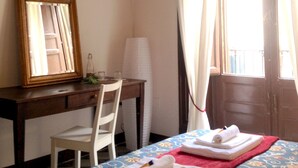 Une chambre d’hôtel avec un bureau en bois, une chaise, un lit recouvert d’une courtepointe à motifs floraux et une fenêtre avec des rideaux.