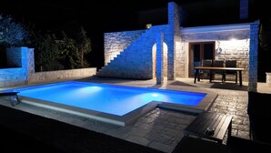 A swimming pool with a stone structure and a table with chairs. - Authentic Dalmatian Getaway • Pool & free parking (Trogir)