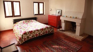 Une chambre à coucher avec un lit, une commode, une cheminée et deux fenêtres.