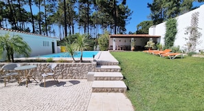 A pool area with a stone wall, outdoor seating, and a grassy lawn. - Architect Villa with private pool, 3 minutes to the beach and 20 min to Lisbon (Verdizela)