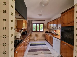 Une cuisine avec des meubles de rangement en bois, un four encastré et une fenêtre avec des rideaux.