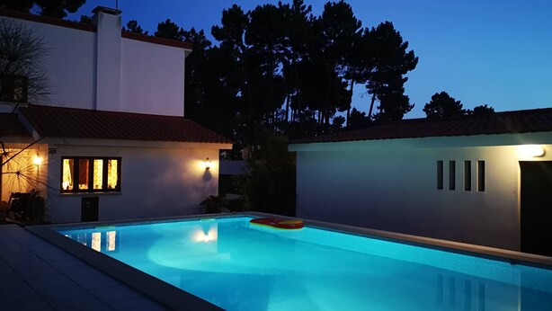 Une piscine à l’eau d’un bleu cristallin, entourée d’un bâtiment blanc surmonté d’un toit recouvert de tuiles rouges.