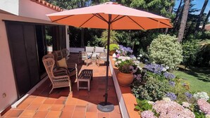 Une terrasse extérieure avec des meubles en osier, une table en bois et un grand parasol orange.