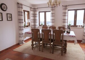 Un coin repas avec une table dressée pour six personnes, entourée de six chaises, et une vue sur la mer grâce à de grandes fenêtres.
