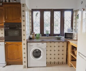 Une cuisine compacte équipée d’un lave-linge, de meubles en bois, d’un four à micro-ondes et d’une fenêtre donnant sur un paysage agréable.