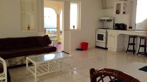 A living room with a brown sofa, a white coffee table, and a view of the outdoors through a doorway. - Beautiful, spacious two bedroom apartment with lovely gardens and awesome views. (Saint John)