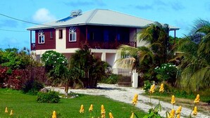 A two-story house with a red and white exterior, surrounded by lush greenery and yellow flowers. - Beautiful, spacious two bedroom apartment with lovely gardens and awesome views. (Saint John)