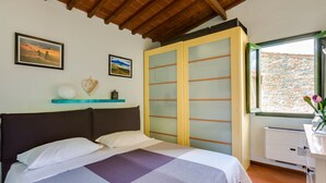 Un dormitorio con una cama, un armario con puertas de vidrio esmerilado, un estante con adornos y una ventana con vistas a un muro de piedra.