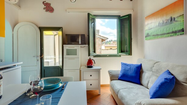 Una habitación compacta con kitchenette, zona de comedor y sofá con cojines azules.