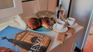 Una habitación con una cama, una mesita de noche con una lámpara, un plato de cruasanes, una taza y un libro.