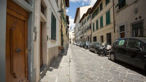 Una estrecha calle adoquinada bordeada por coches estacionados y edificios con contraventanas verdes.