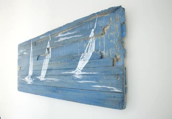 Un panel de madera grande y rústico con un acabado azul desgastado y pinturas de veleros blancos.