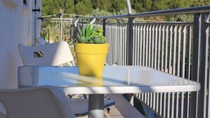 Een balkon met een witte tafel en stoelen, een gele plant in pot en een metalen hekwerk.