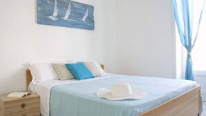 Een slaapkamer met een bed, een nachtkastje, een blauw schilderij en een witte hoed op het bed.